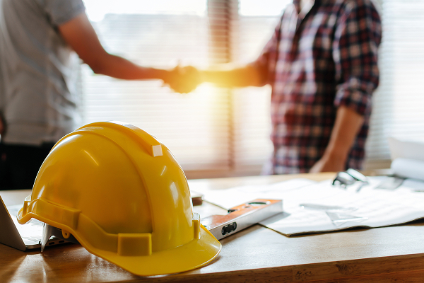 Contractors shaking hands with yellow hard hat on desk, symbolizing general liability insurance