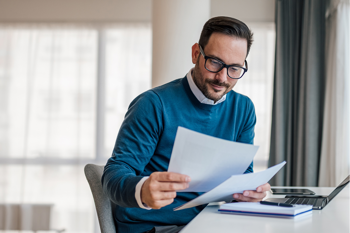 Man wearing glasses reading papers in his hand