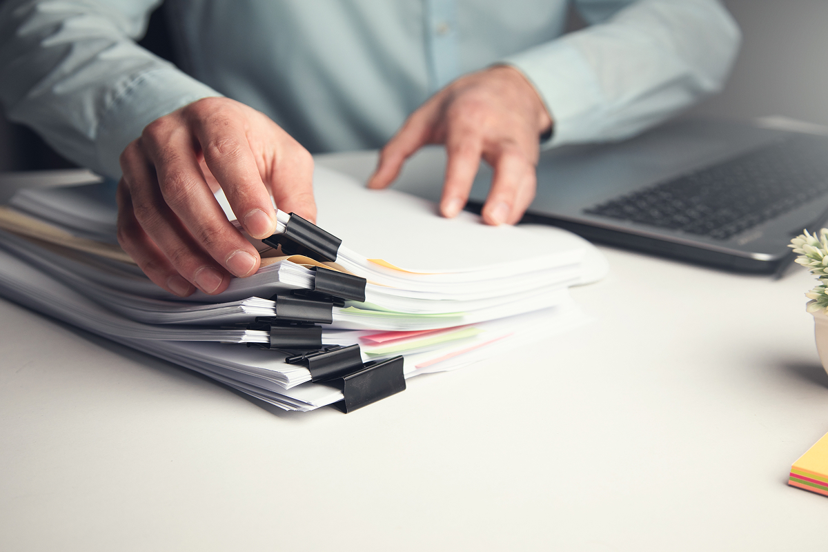 A man is picking up a bundle of papers from a stack
