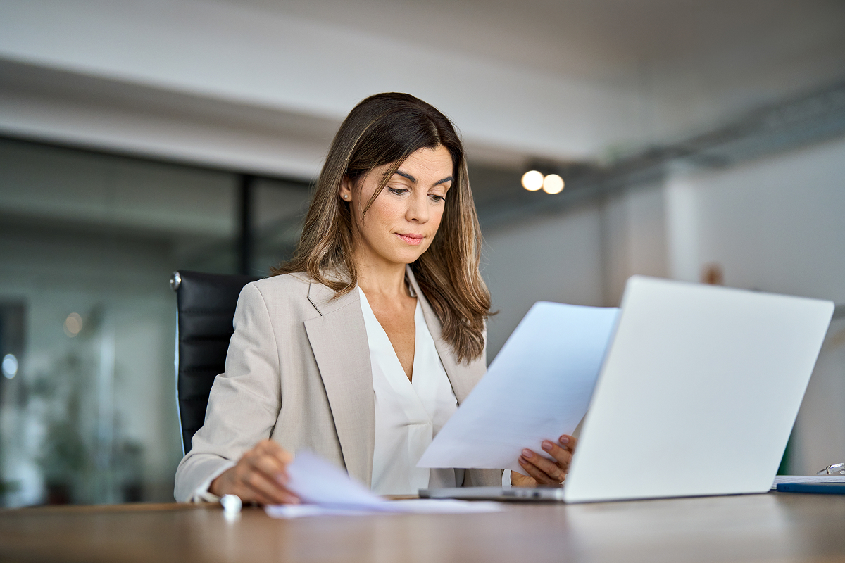 A woman wearing a blazer, scanning papers and a computer screen
